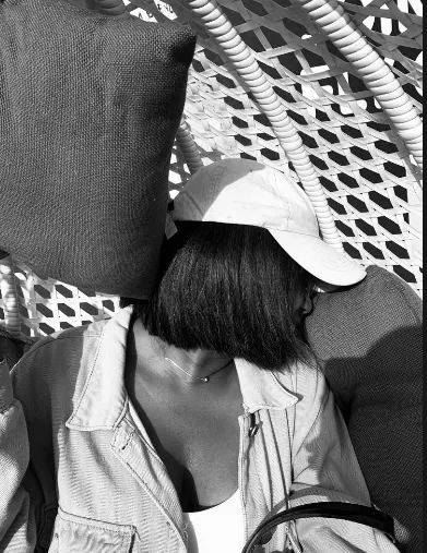 Busayo in a cap, resting in a woven chair